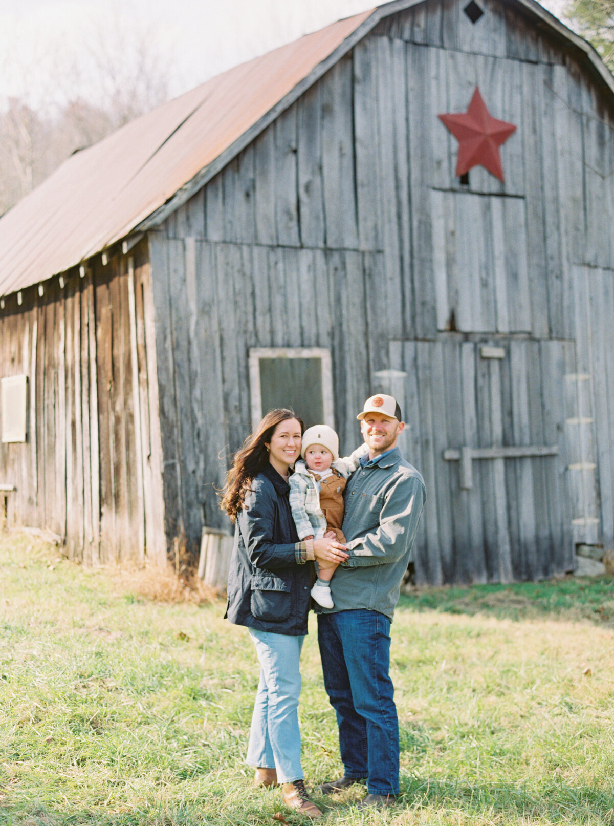 Madison with her husband and their baby in front of an old barn